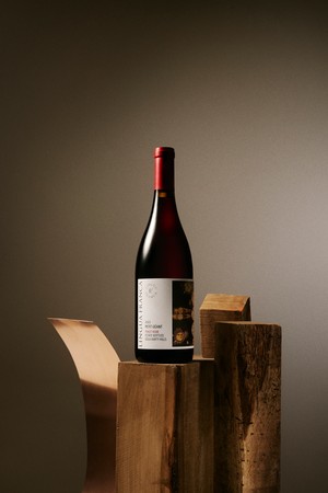 A bottle of 2022 Petit Geant Pinot Noir sits on a wooden tree stump